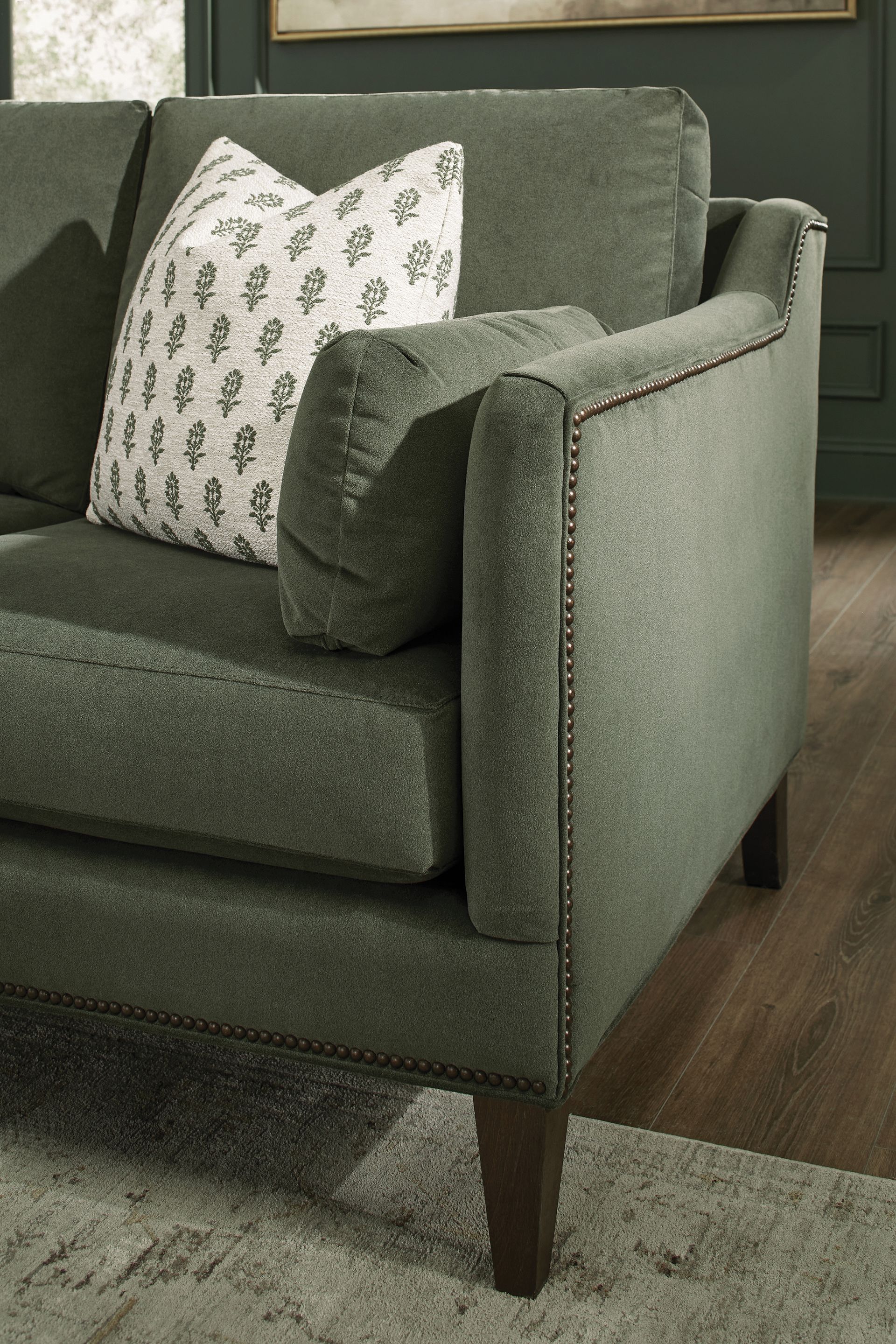 Green sofa with patterned pillow and dark wooden legs.