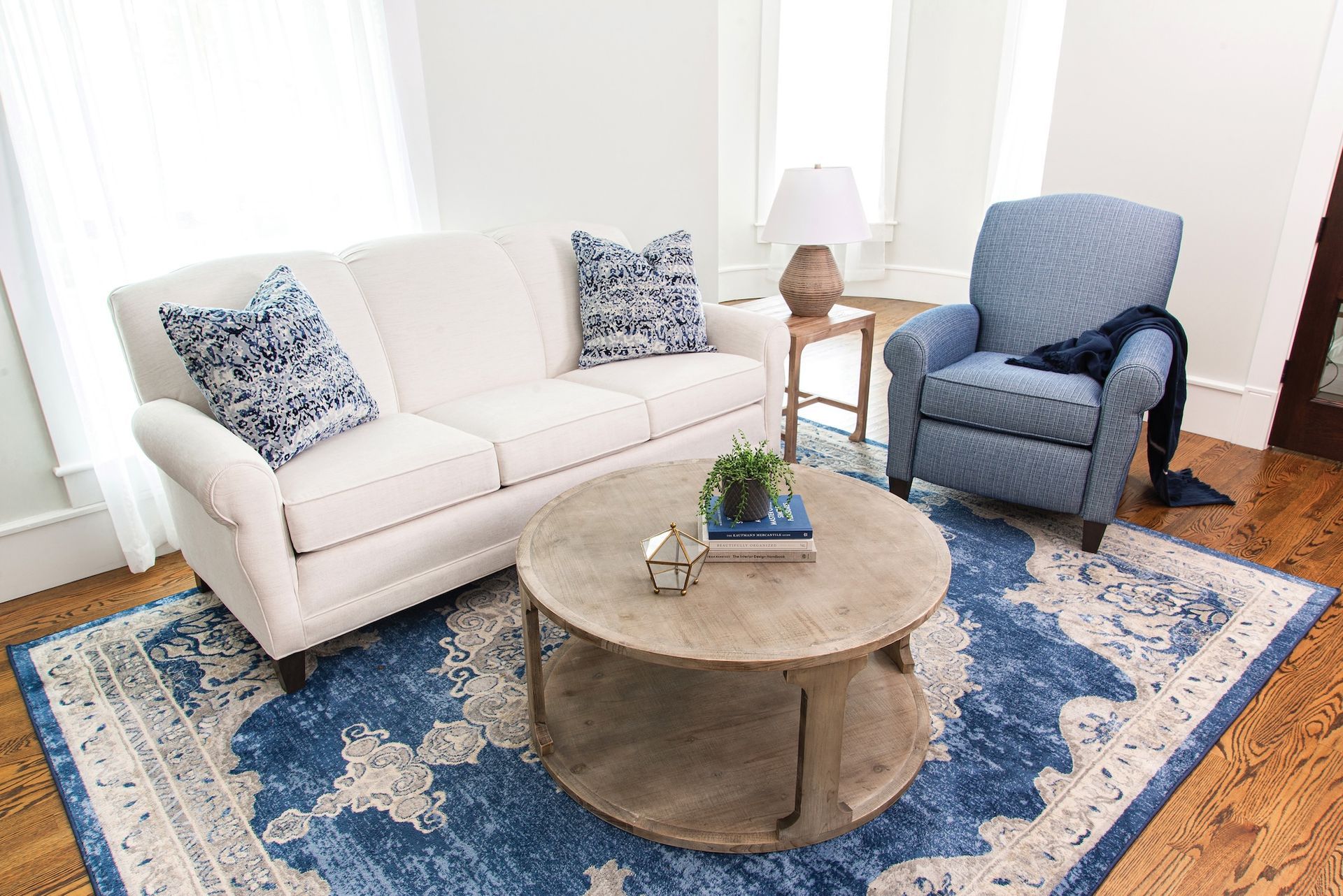 Living room with white sofa, blue armchair, round coffee table, and blue patterned rug.