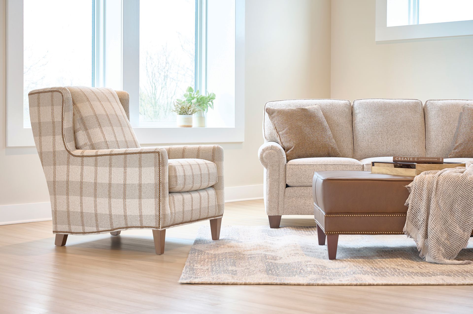 Living room with plaid armchair, sofa, ottoman, and rug near a window.