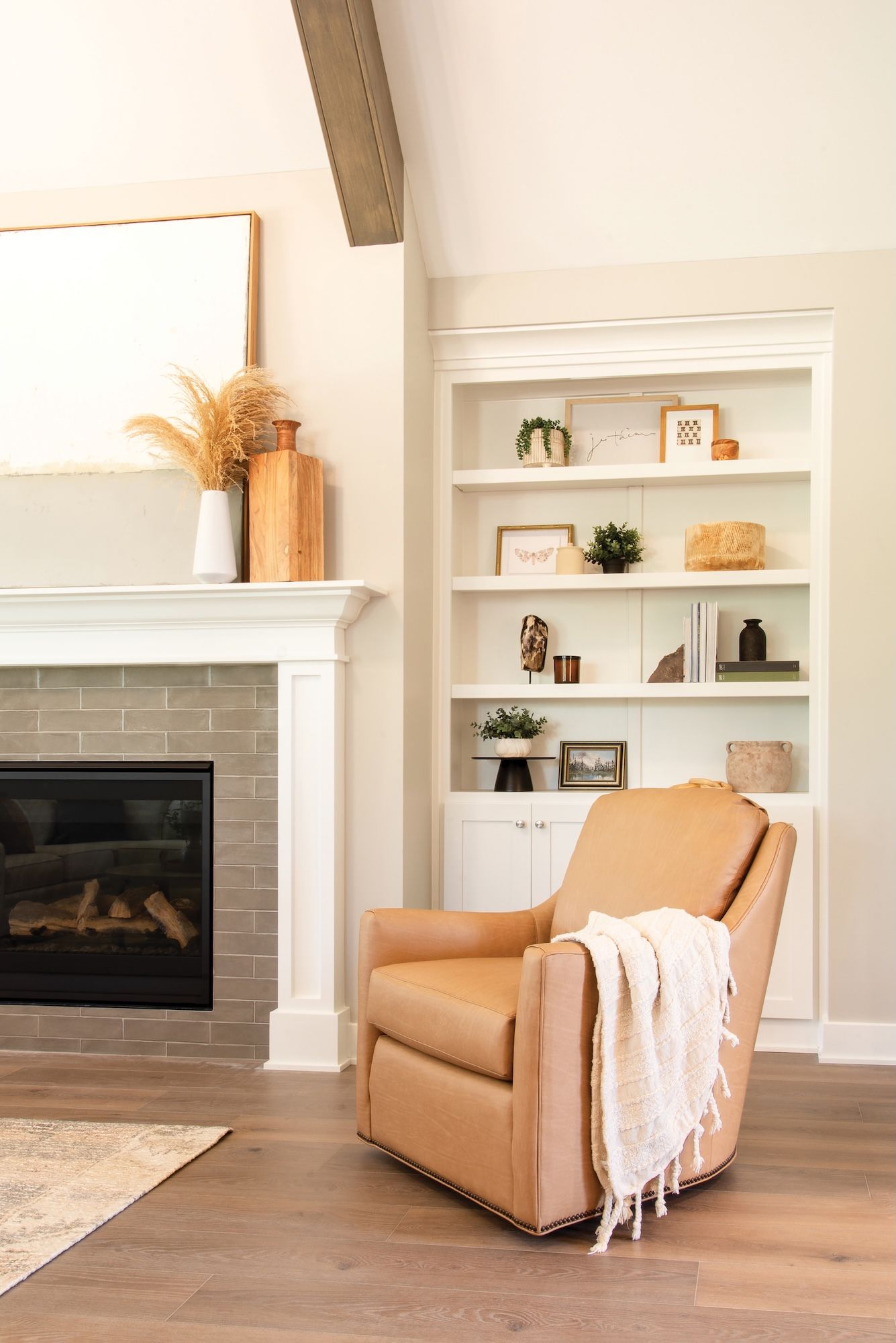 Cozy living room with tan leather armchair, fireplace, and built-in white bookshelf filled with decor.
