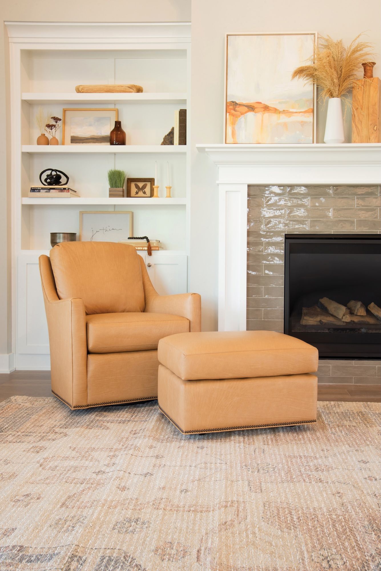 Tan leather chair and ottoman on a patterned rug, next to a fireplace and built-in bookshelf.