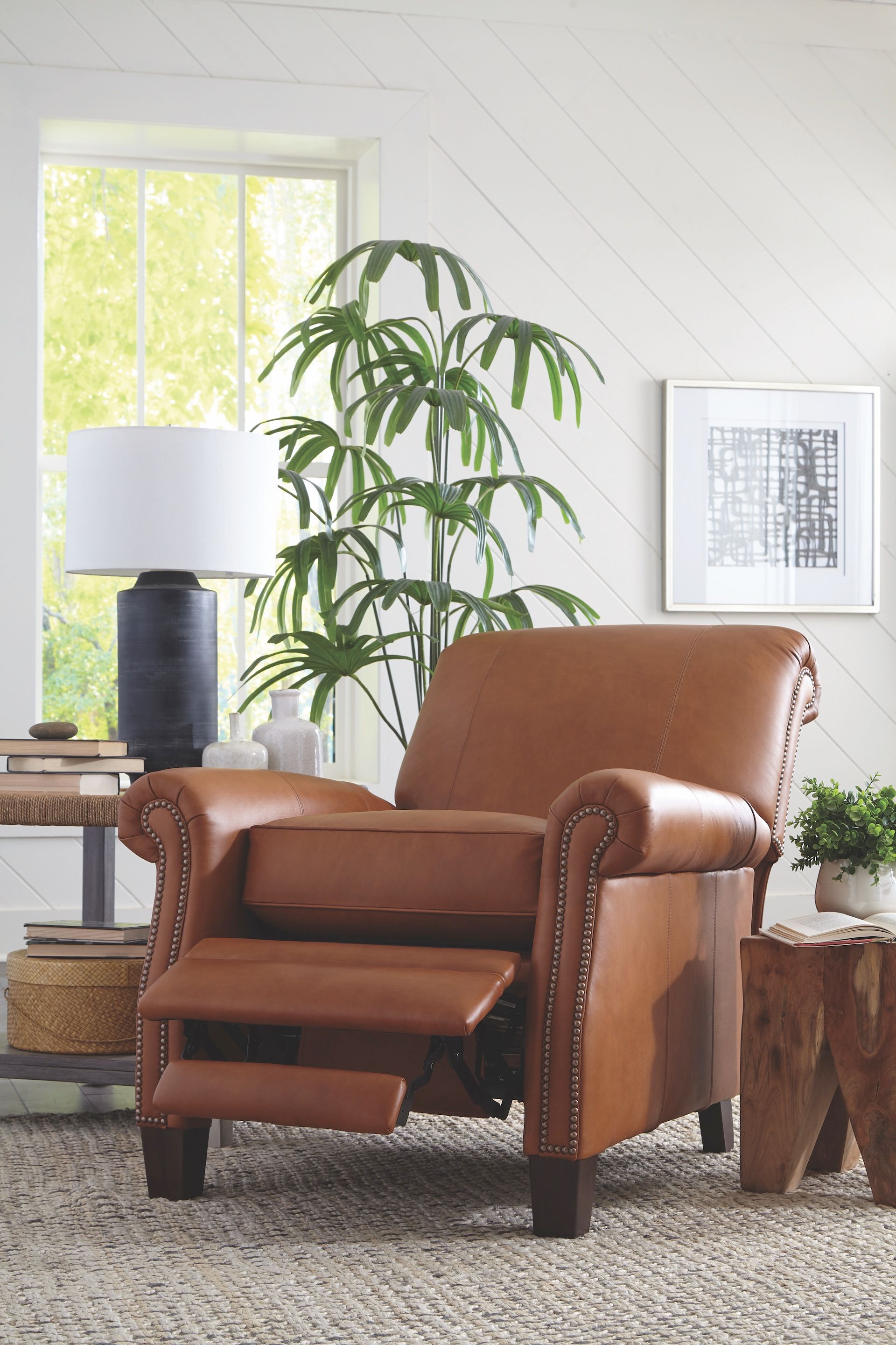 Brown leather recliner chair in a well-lit room with a plant, lamp, and side table.