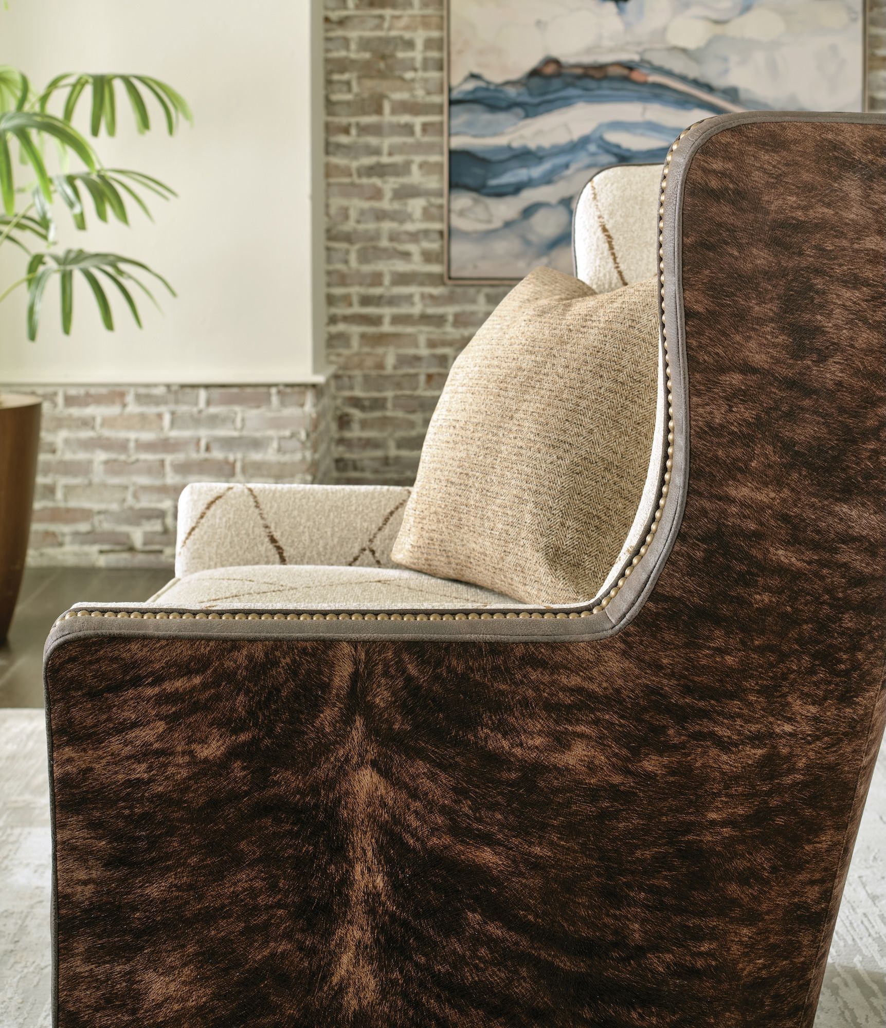 Brown cowhide-patterned armchair with studded trim, a tan pillow, and neutral walls.
