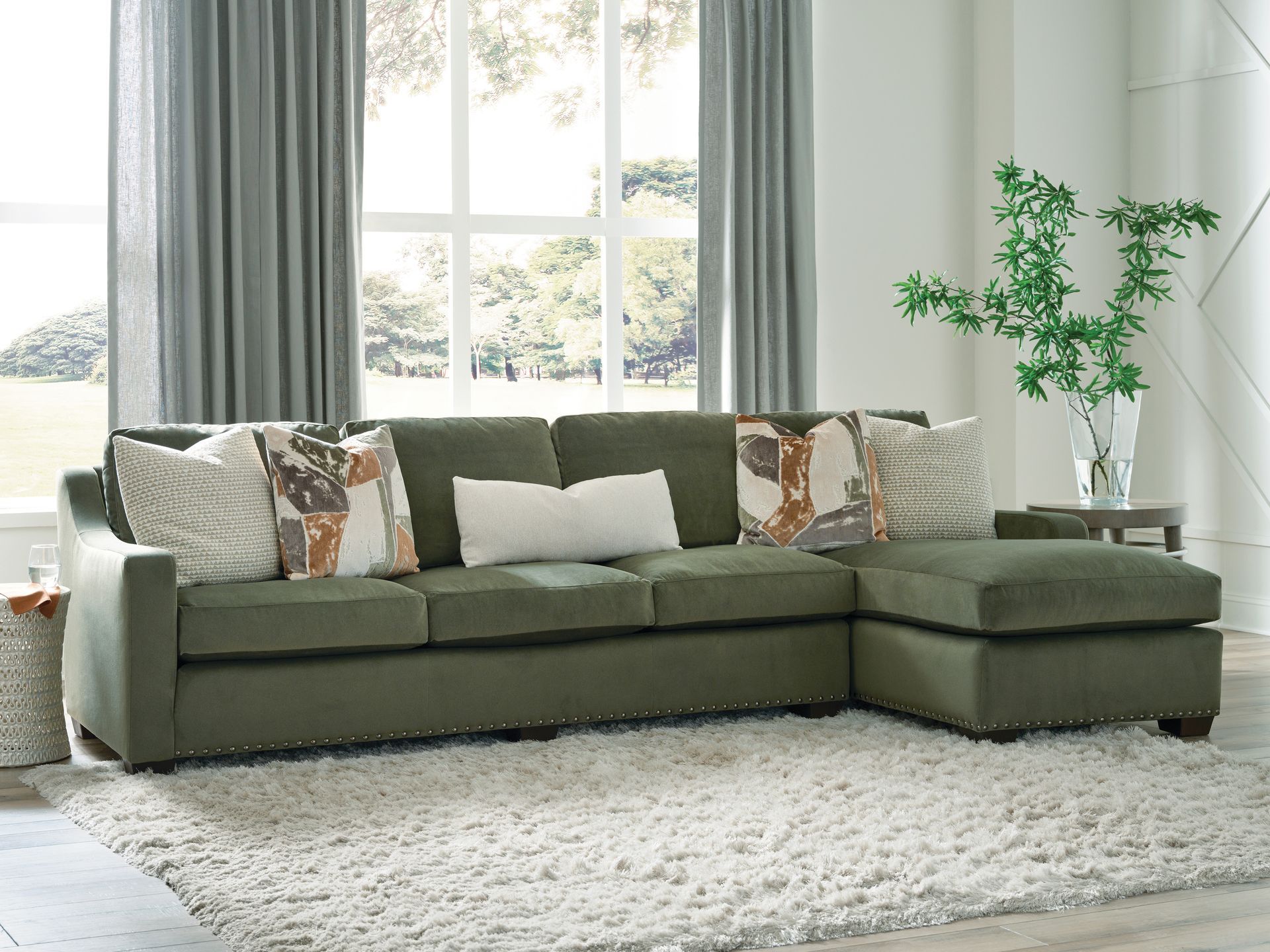 Green sectional sofa with ottoman in a living room, accented by patterned pillows and a shaggy rug.