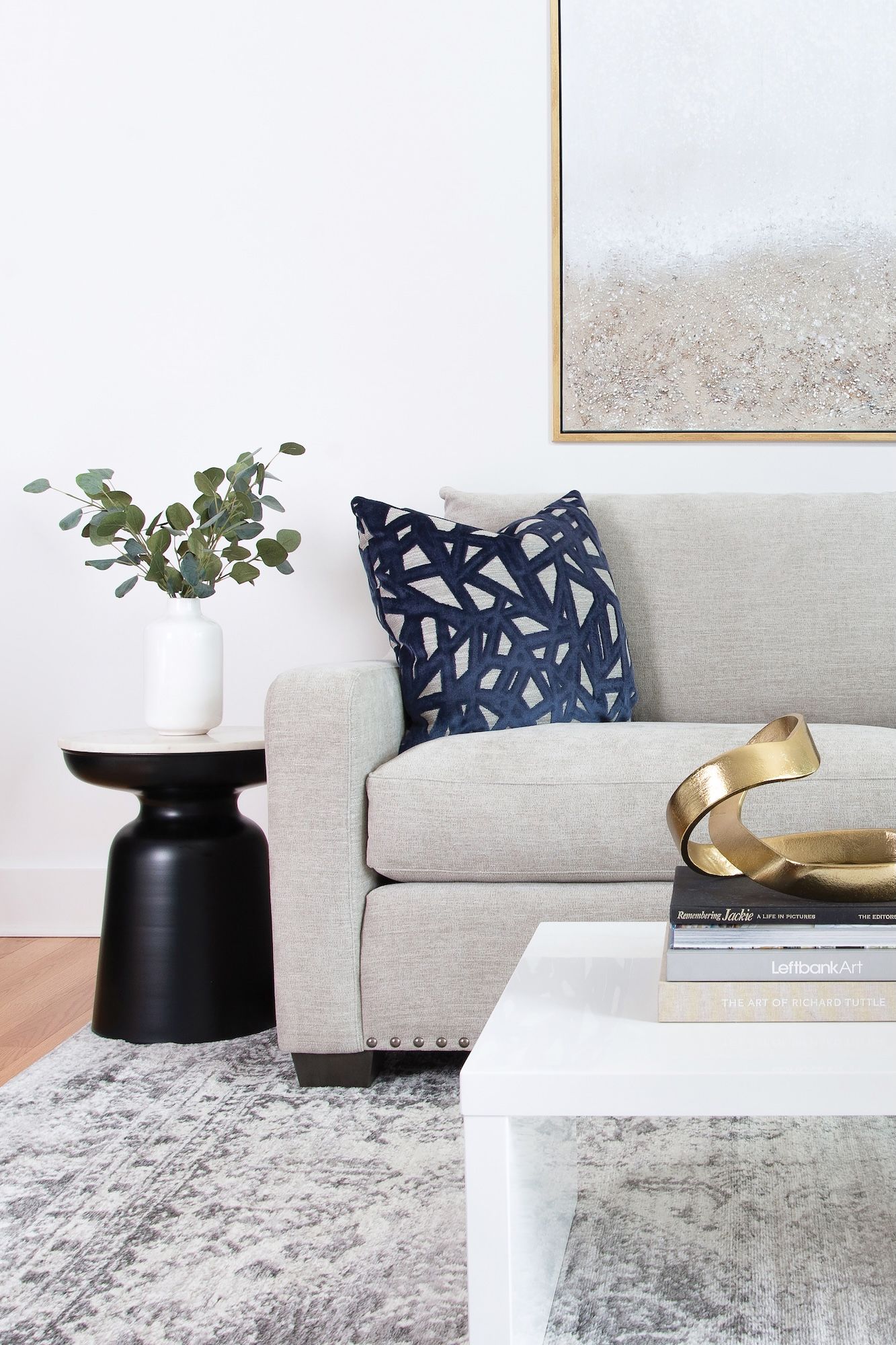 Living room with gray sofa, patterned pillows, white coffee table, and black side table with plant.