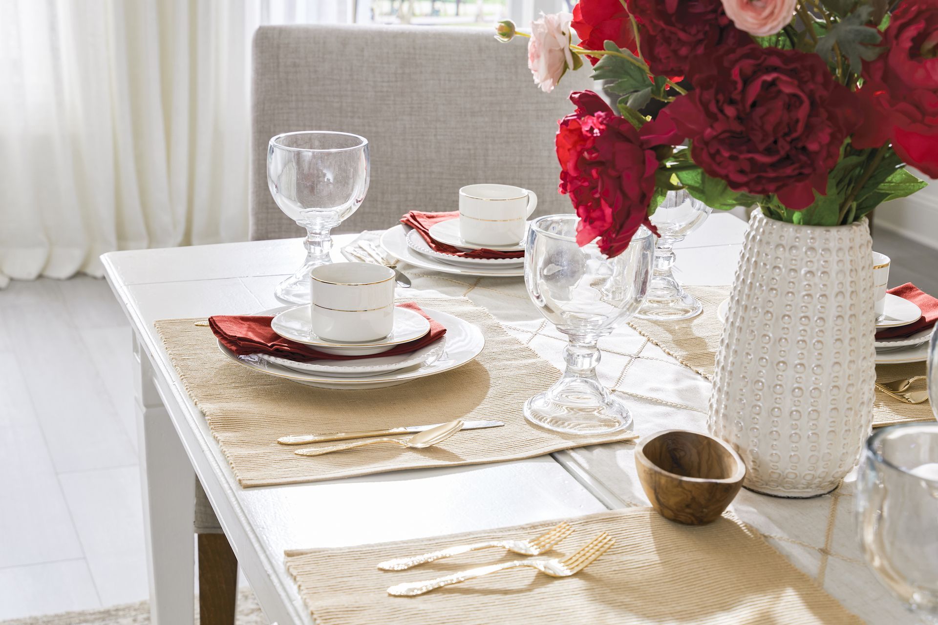 White dining table set for a meal, with floral arrangement in a white vase.