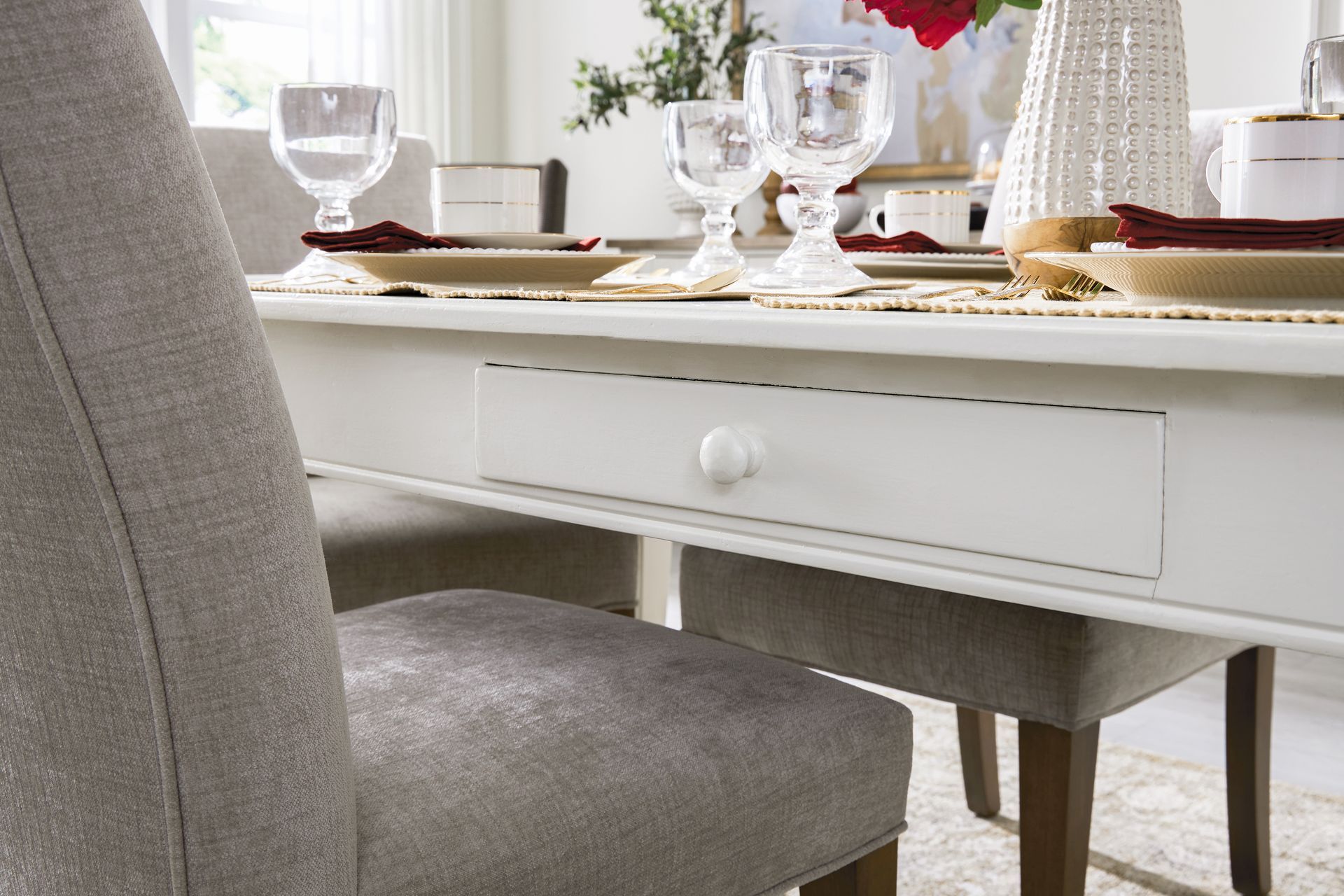 White dining table with drawer, set for a meal. Grey upholstered chairs sit around the table.