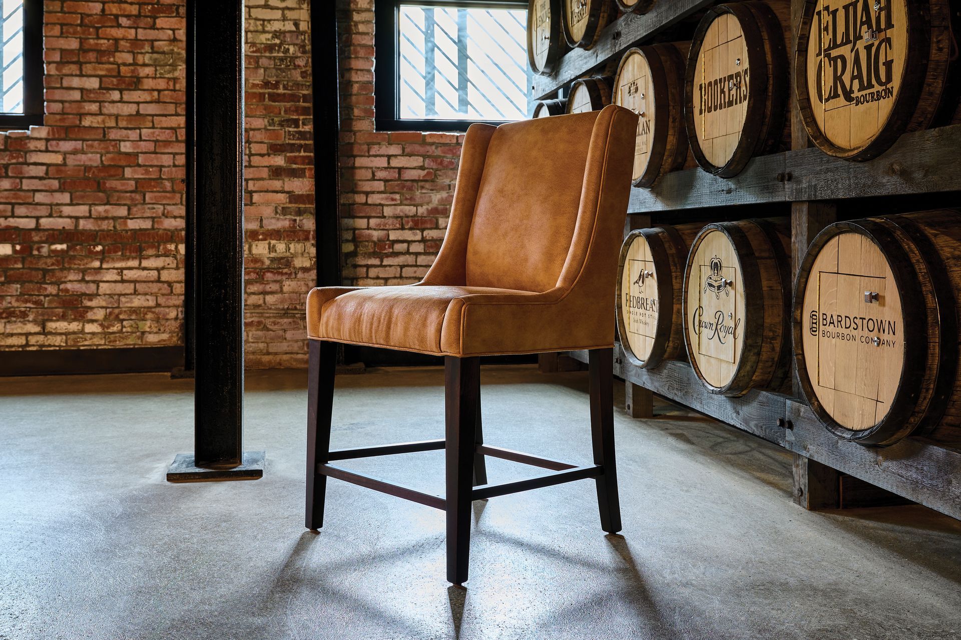 Leather bar stool in a distillery, barrels in background, exposed brick and beams.