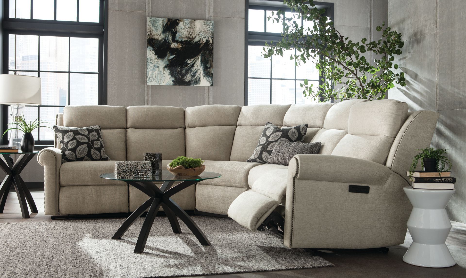 Beige sectional sofa in a living room with end tables, a coffee table, and large windows.