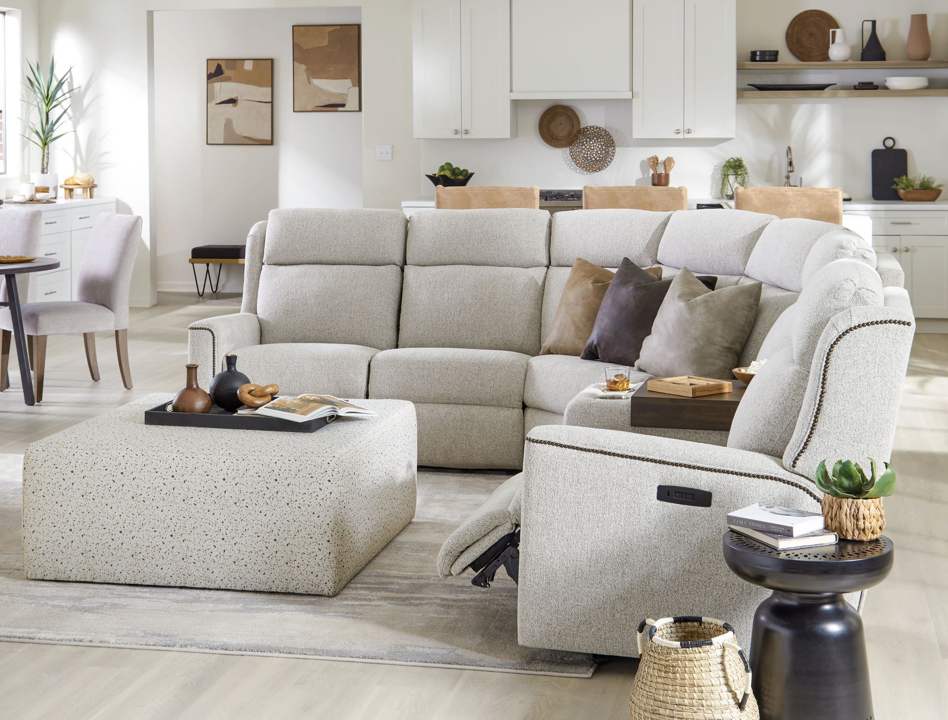 Sectional sofa and ottoman in a living room, with side table, kitchen in background.