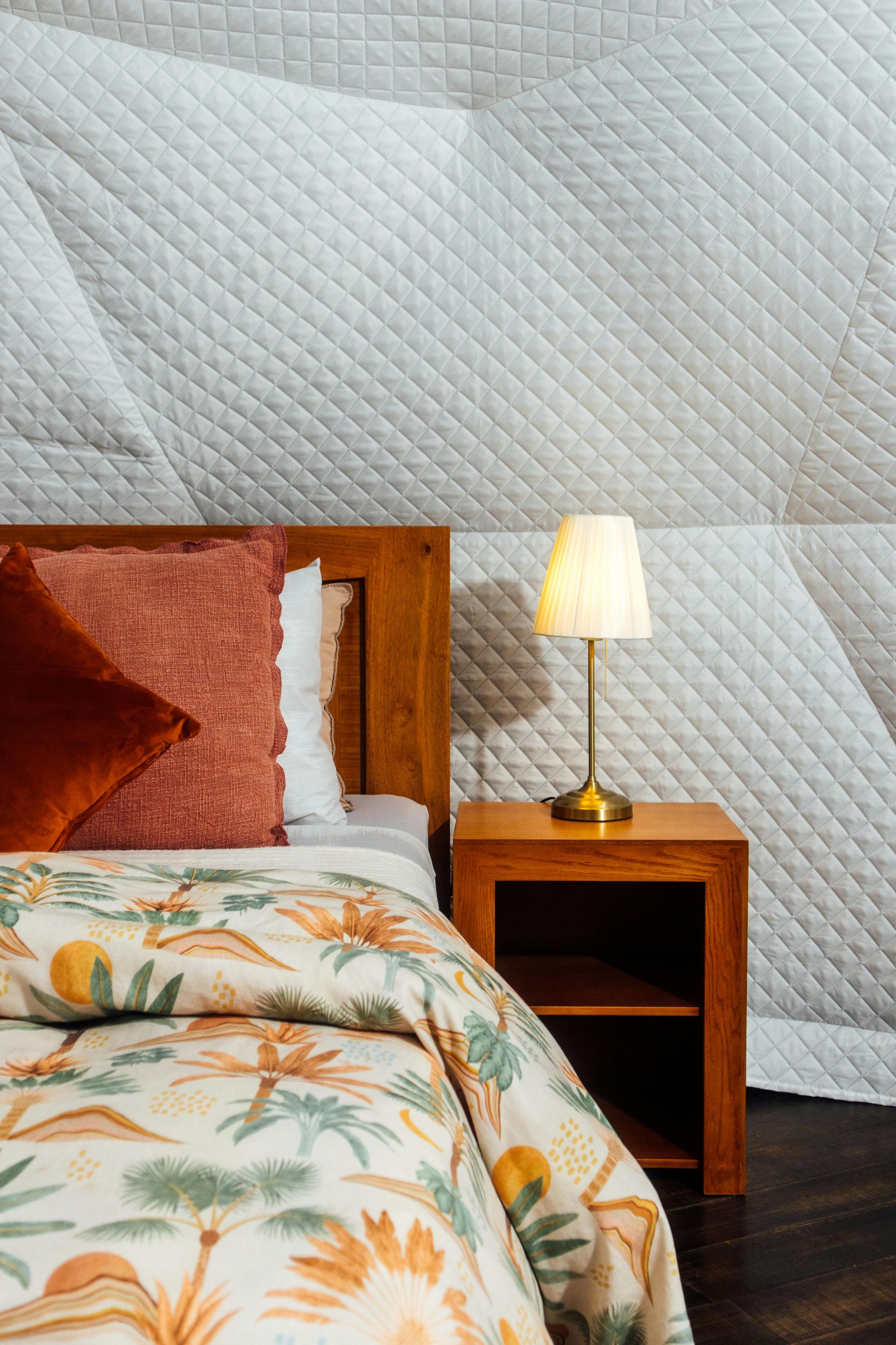 Bedroom interior with bed, nightstand, lamp, and quilted wall.