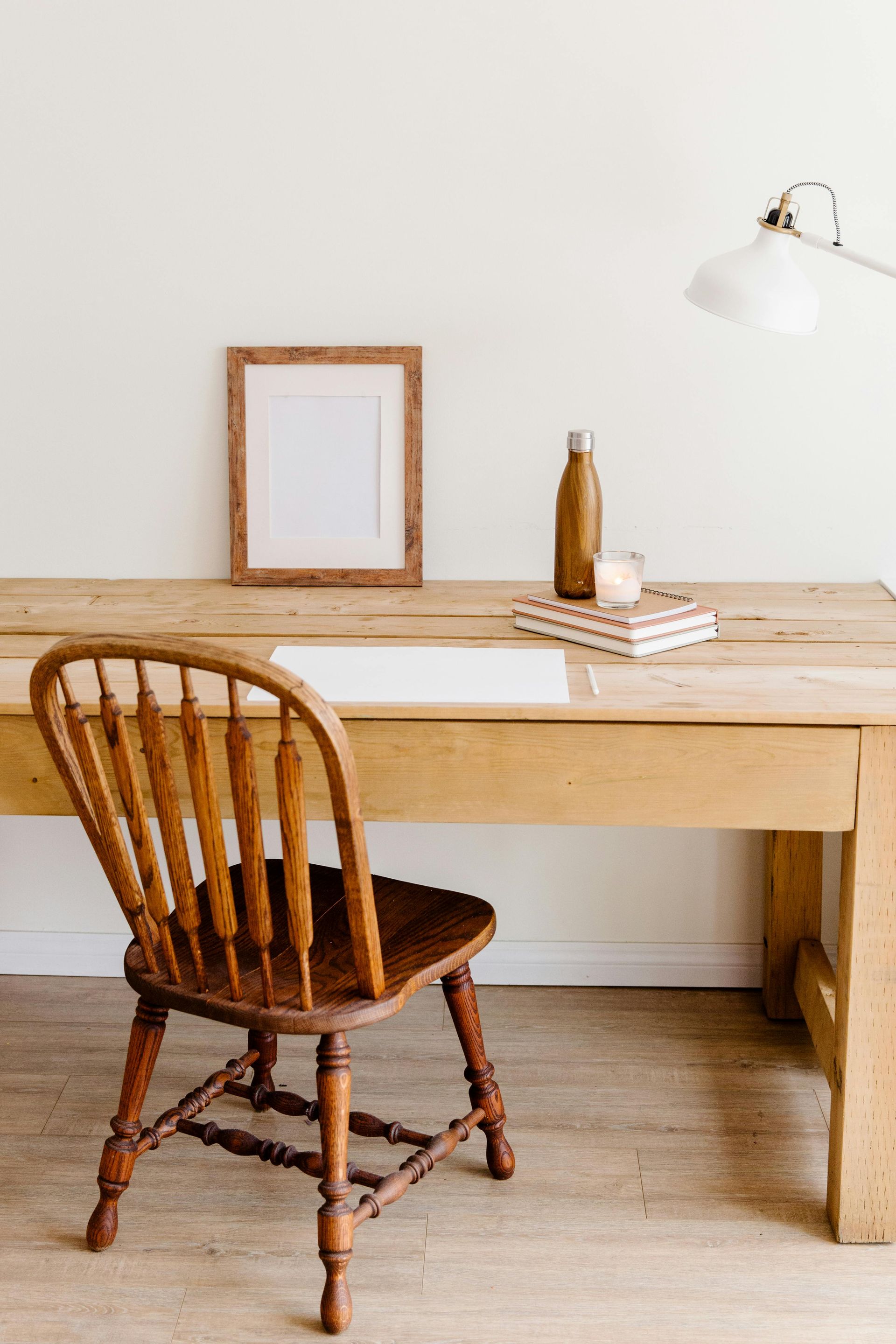 Wooden desk with a chair, framed picture, lamp, water bottle, and books.