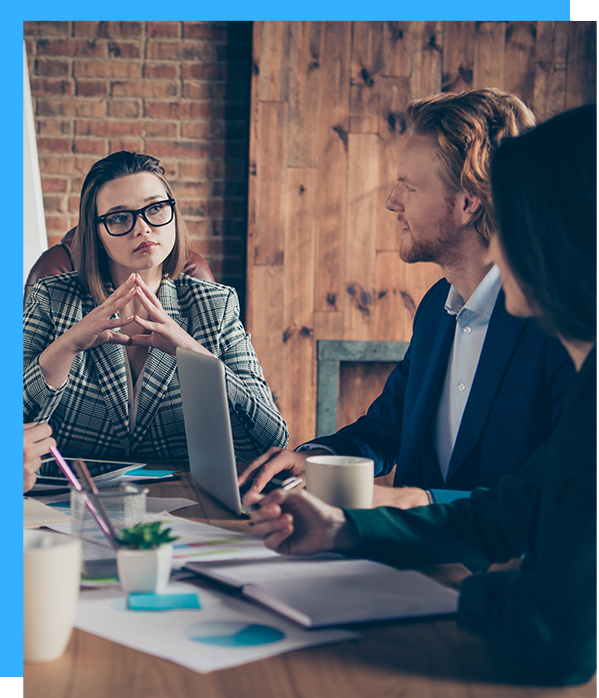 Business meeting: woman in glasses considers, man speaks, documents and laptop on table.