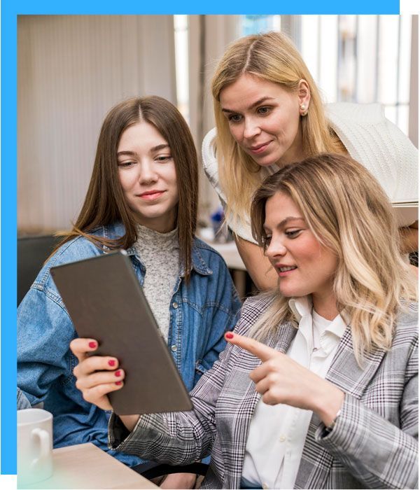 Three women looking at a tablet together in an office; woman points, others smile.
