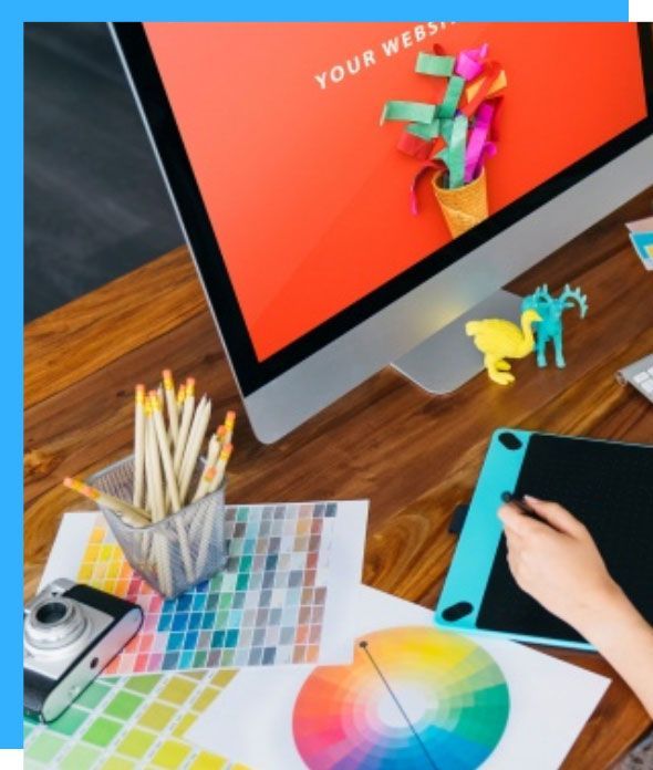 Desk with computer displaying website design, color swatches, and drawing tablet; hand using stylus.