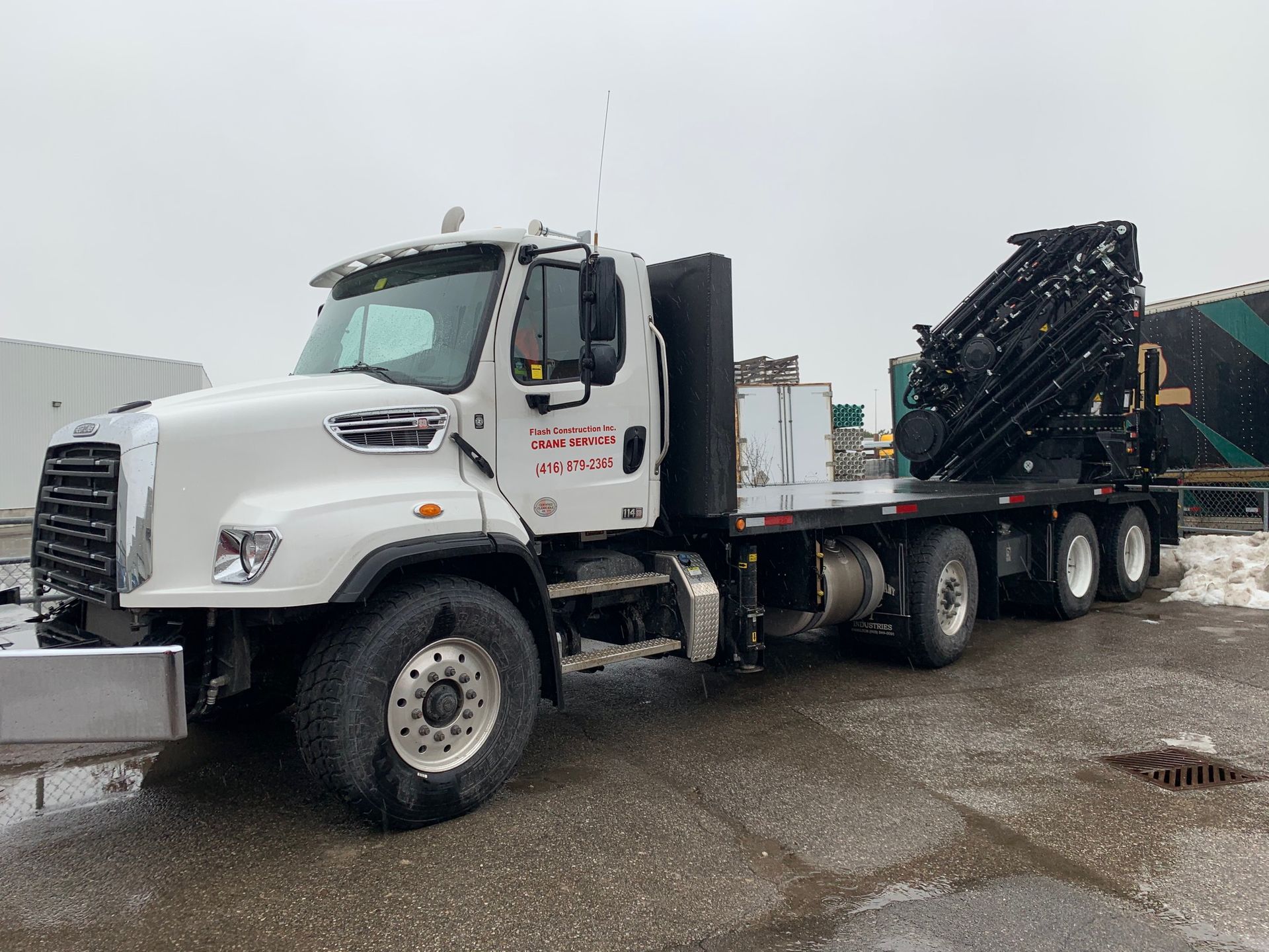 A flatbed truck with a crane attached to the back is parked in a parking lot.