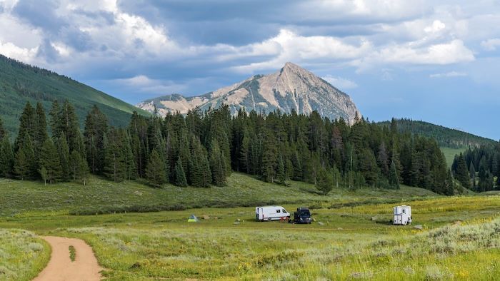 Mountain peak above pine forest and meadow with parked vehicles | Stang Auto Tech in Broomfield, CO