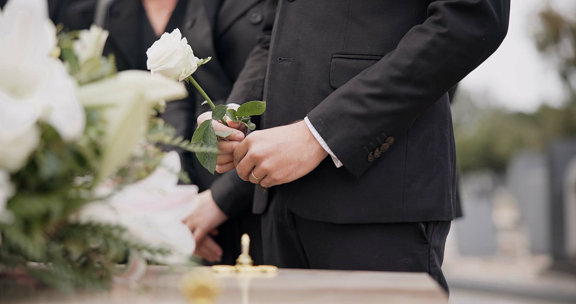 A man in a suit is sitting at a coffin at a funeral.