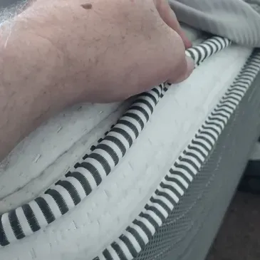 A person is holding the edge of a mattress with their hand.