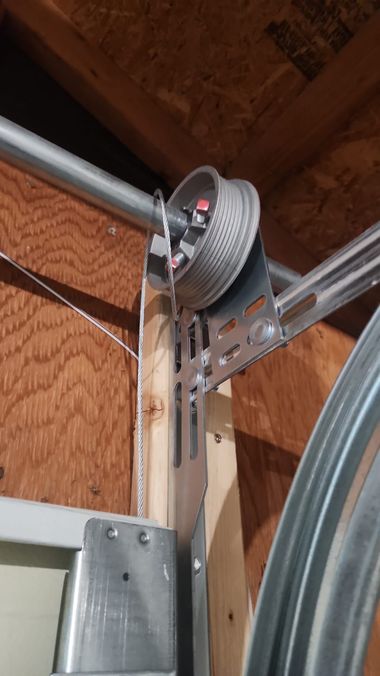 Close-up of a garage door opener trolley and wheel assembly on metal tracks inside a garage.
