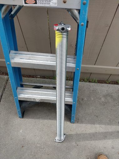 Silver coiled metal spring leaning against a blue step ladder outdoors on concrete.