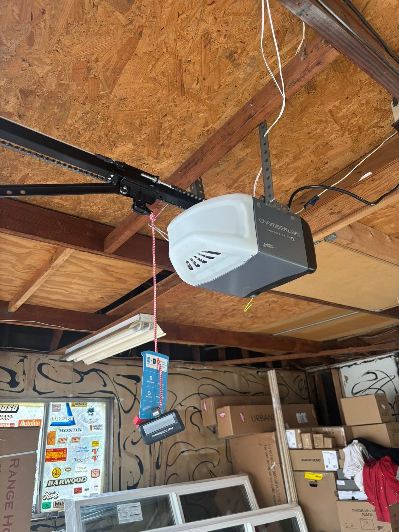 Garage ceiling with a white garage door opener, exposed beams, boxes, and hanging cords