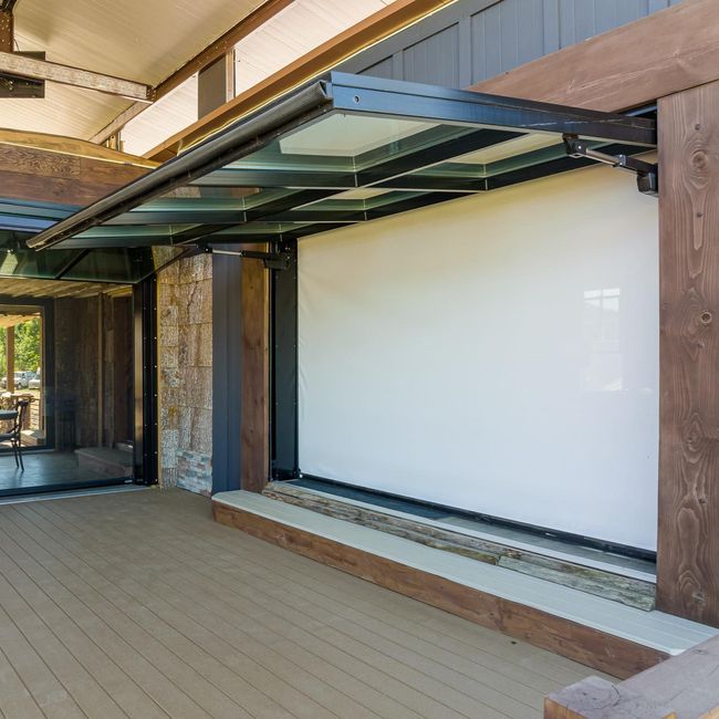 Covered outdoor patio with a glass awning, tiled floor, and a large blank white wall.