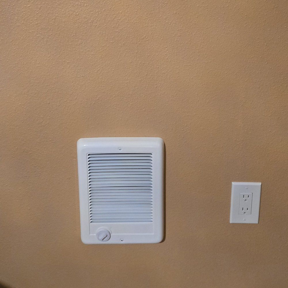 A white fan is mounted on a tan wall next to an electrical outlet.