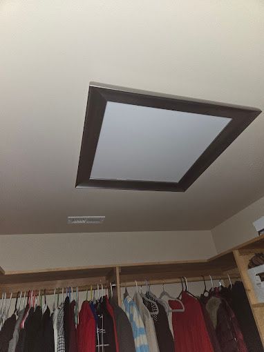 A closet filled with clothes and a square light on the ceiling.