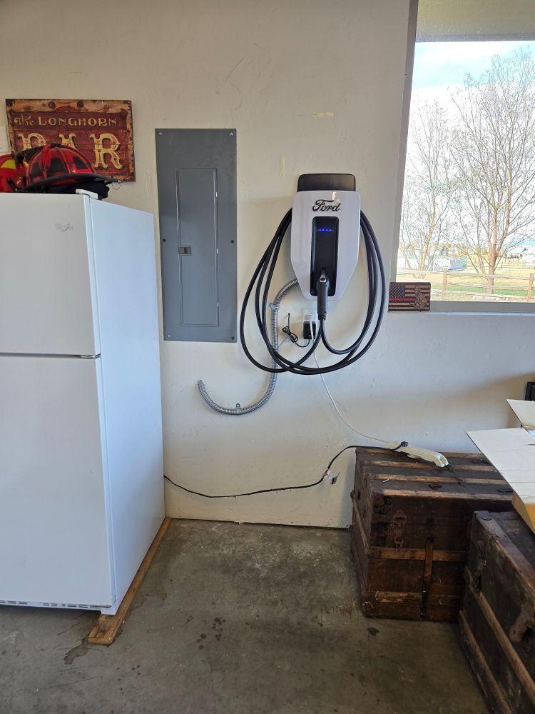 A white electric car charger is hanging on a wall next to a refrigerator.
