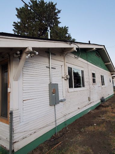 A white house with a green roof has a electrical box on the side of it.