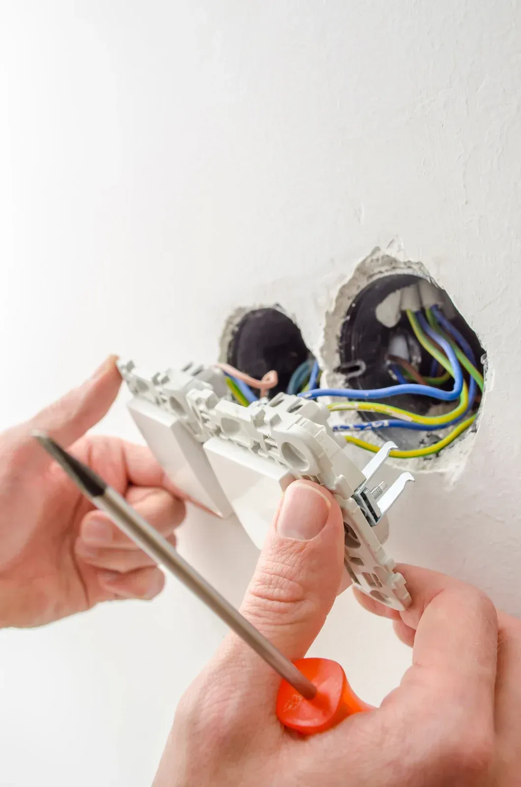 A person is fixing a light switch with a screwdriver.