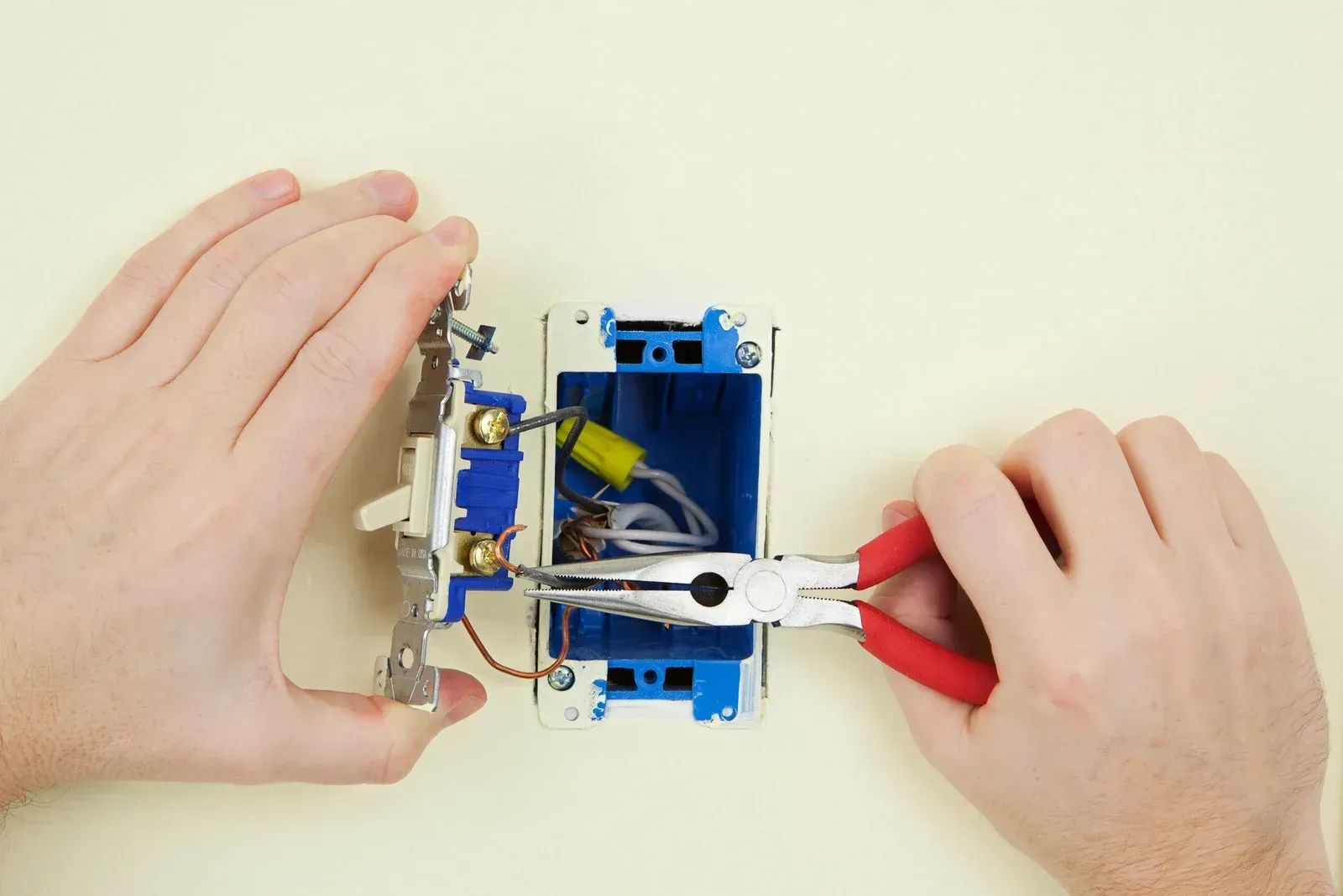 A person is using a pair of pliers to fix a light switch.