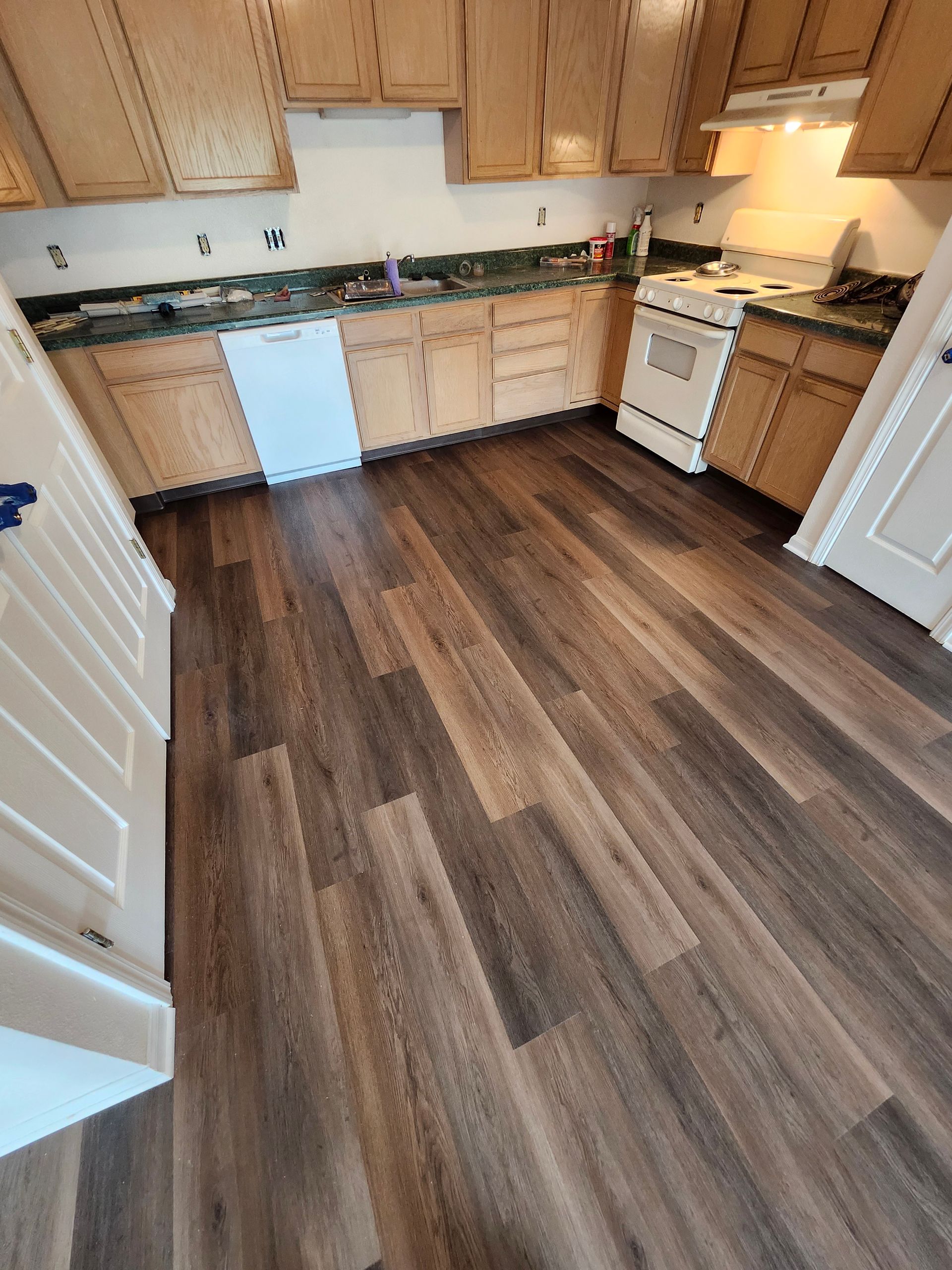 Empty kitchen with light wood cabinets, white appliances, and dark wood flooring.