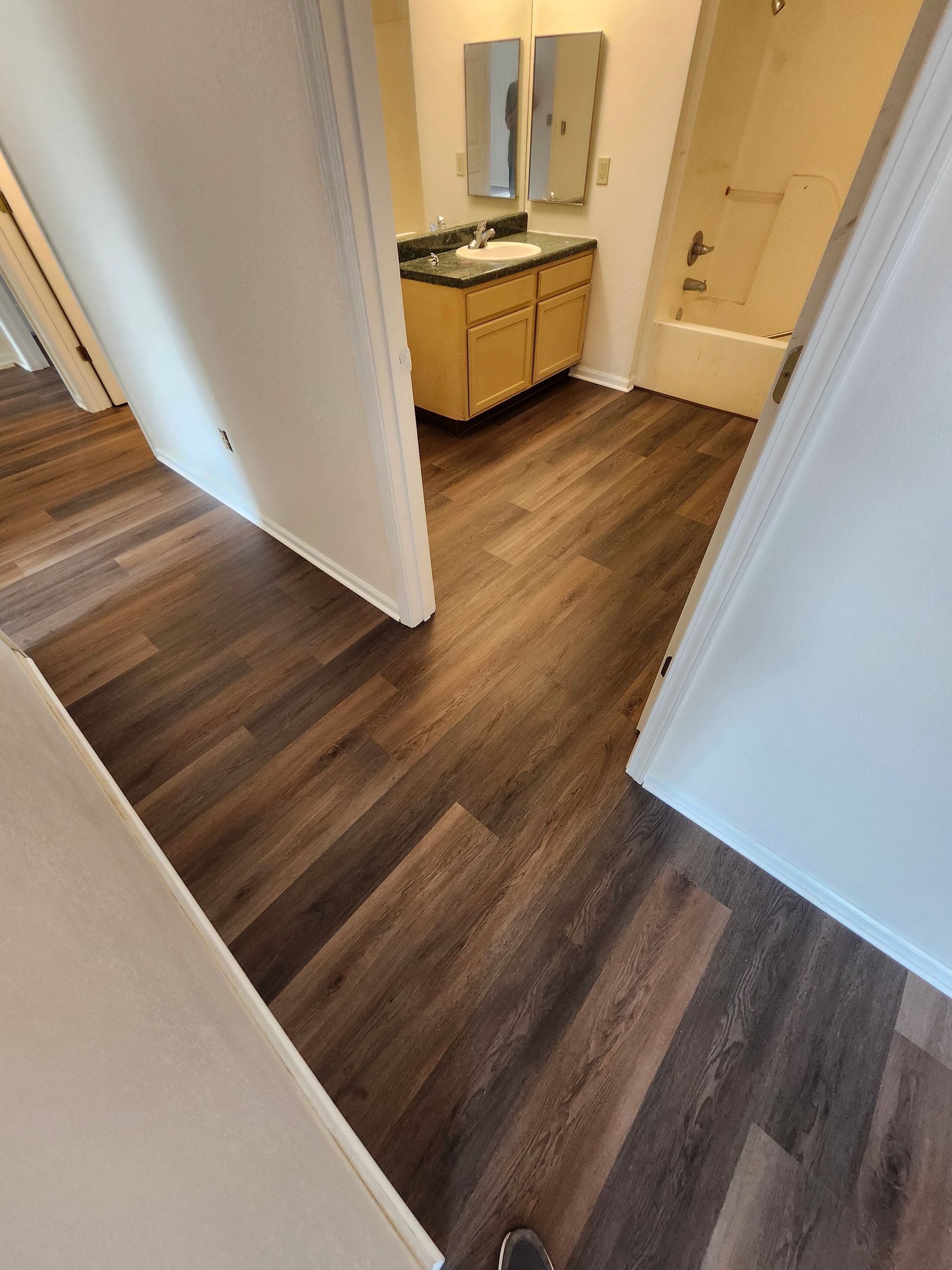 Hallway with dark wood floors leading to a small vanity table and a closed door.