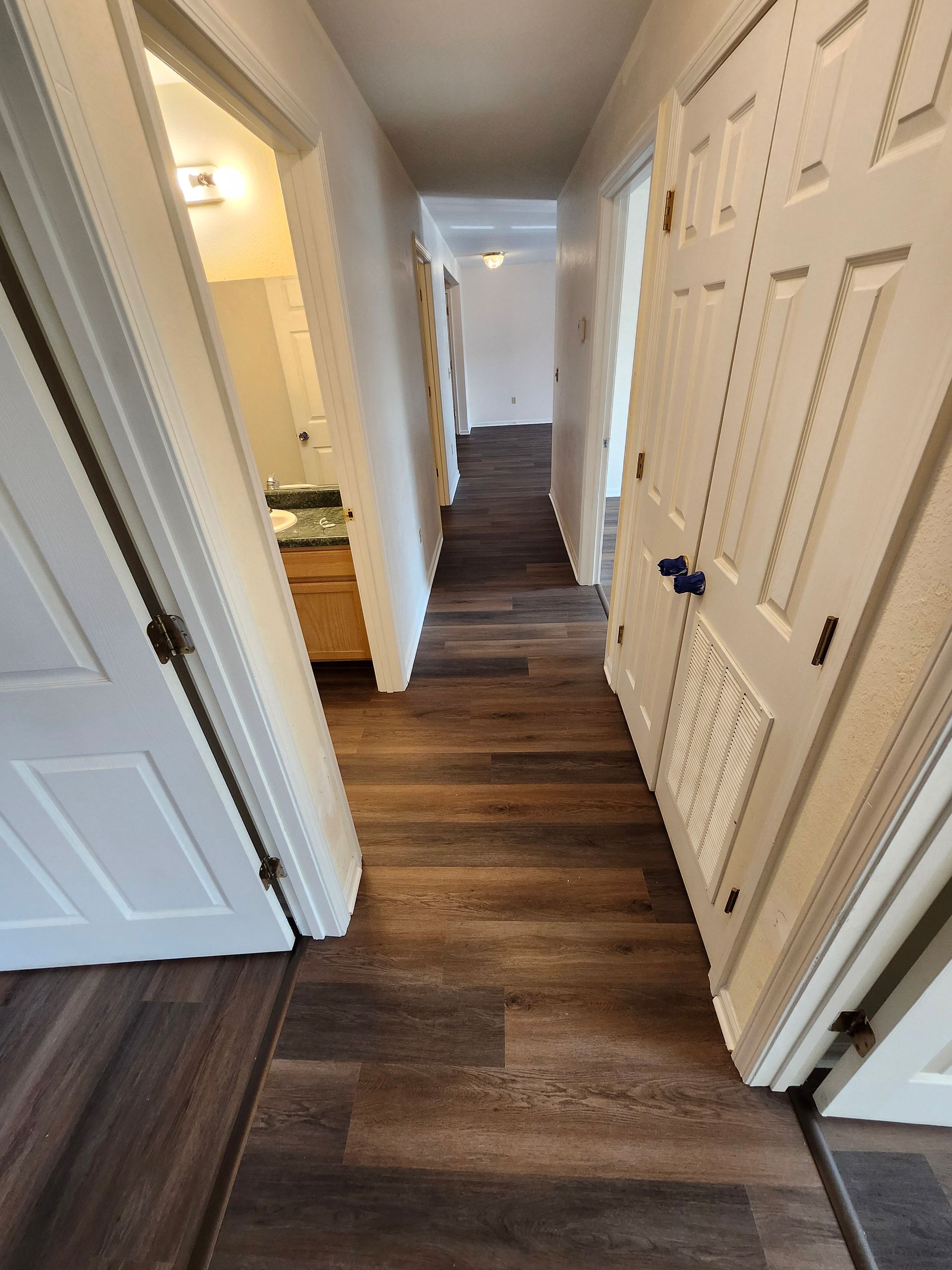 Narrow hallway with dark wood floors, white doors, and a staircase at the far end.