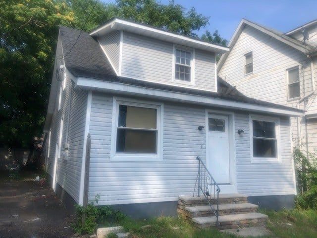 A white house with a black roof and stairs in front of it.