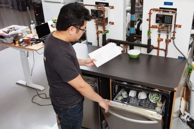 A man is opening a dishwasher with a piece of paper in his hand.