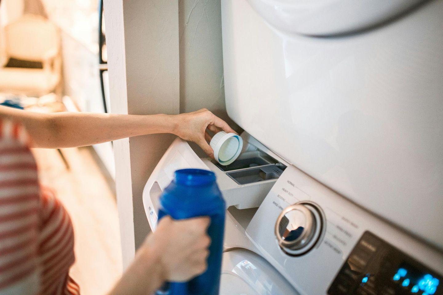 A woman is pouring laundry detergent into a washing machine.