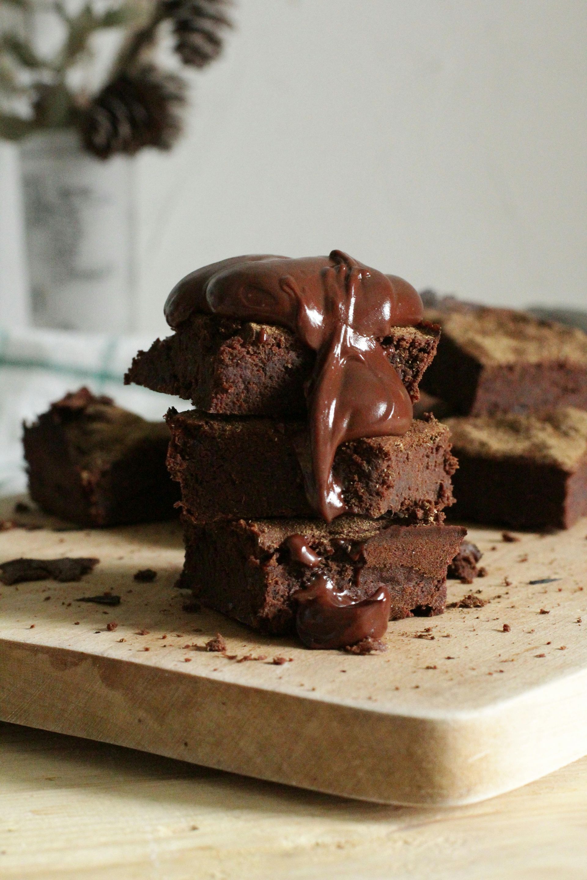 A stack of brownies covered in chocolate sauce on a wooden cutting board.