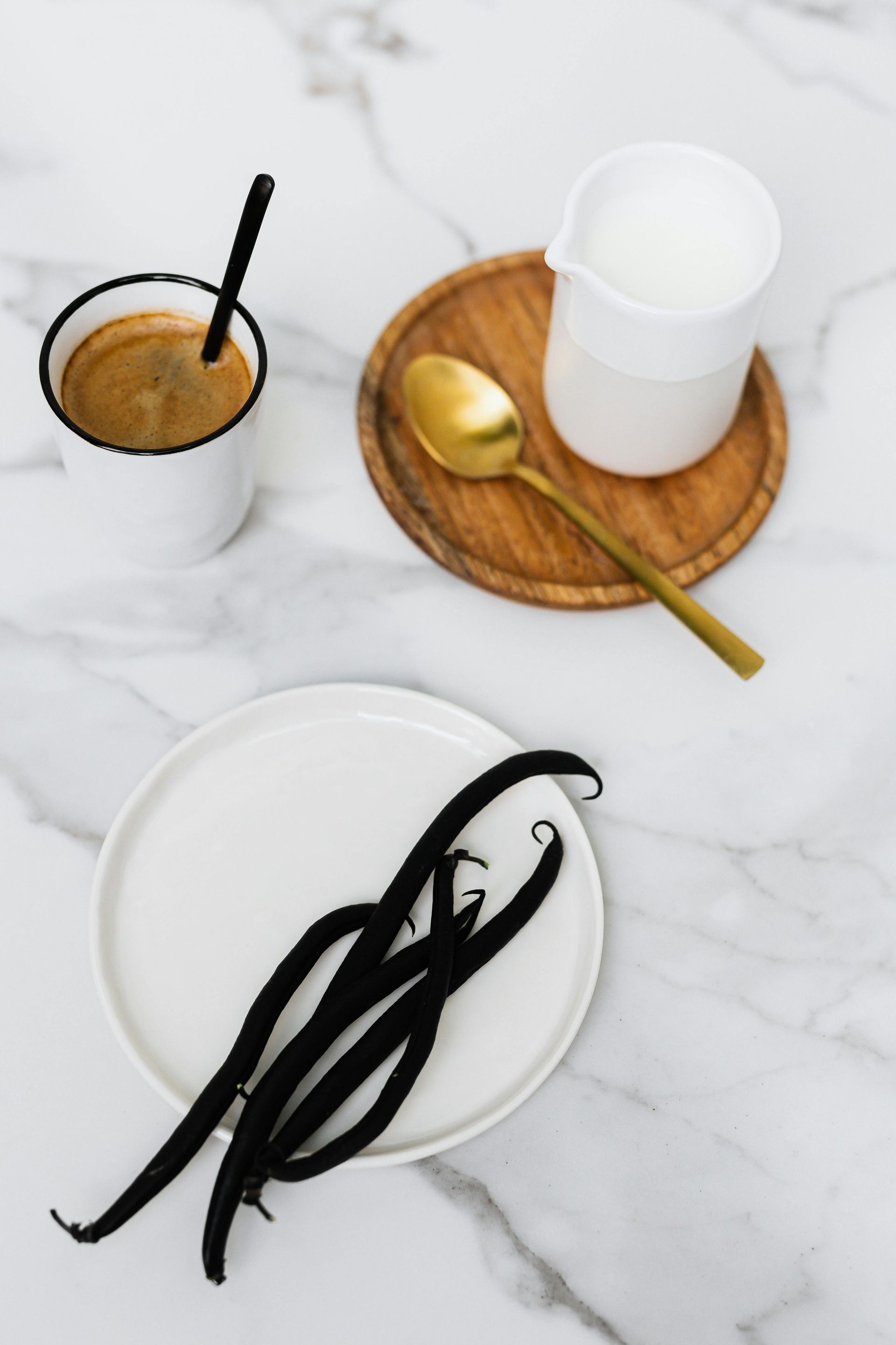 Vanilla beans on a plate next to a cup of coffee