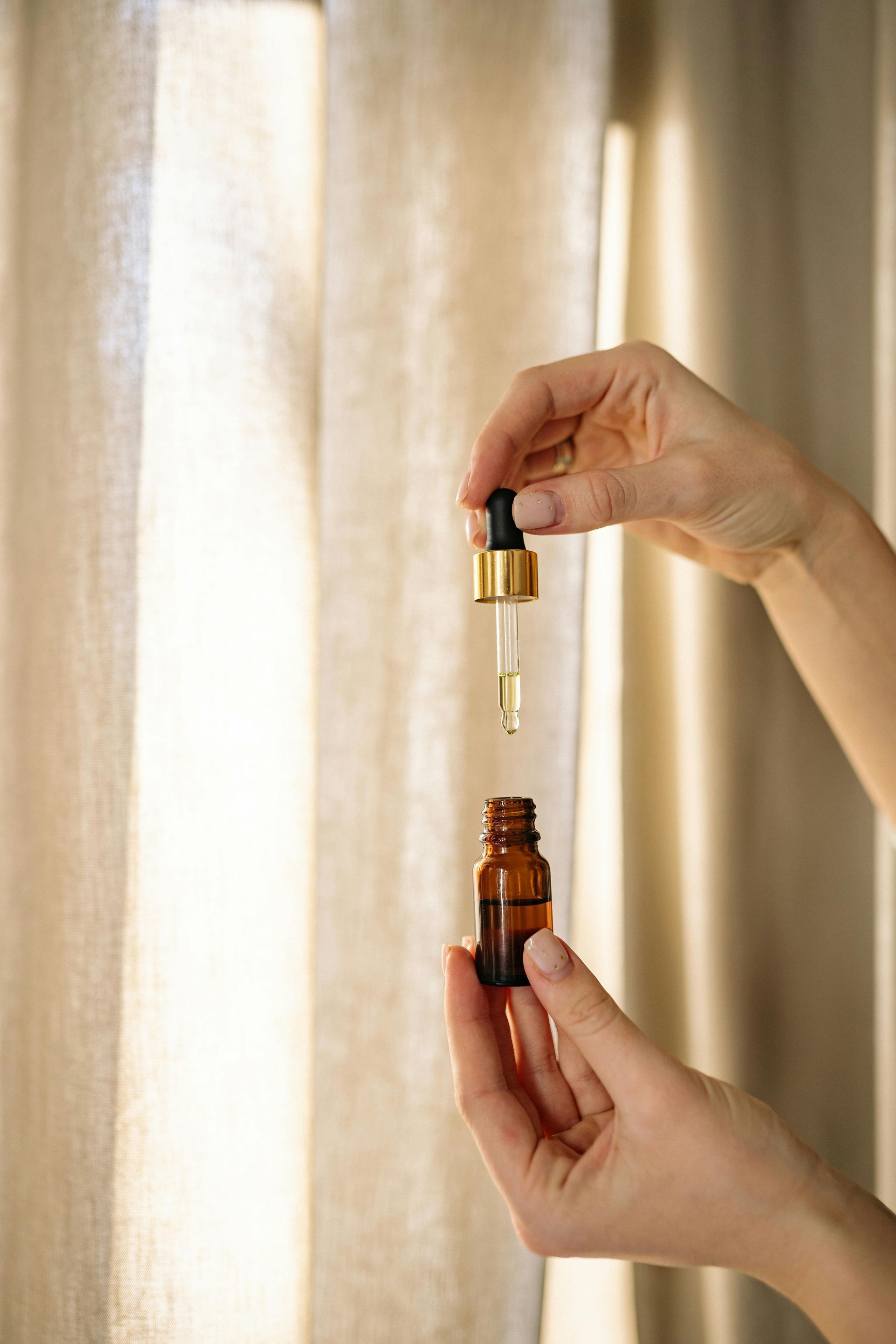 A woman is holding a bottle of essential oil with a pipette.