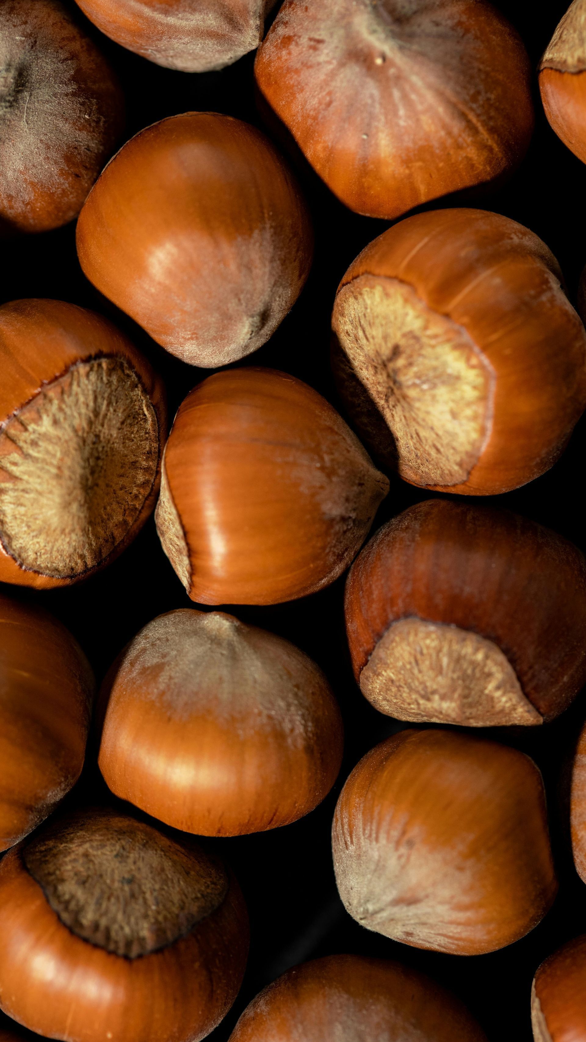 A close up of a pile of hazelnuts on a black surface.