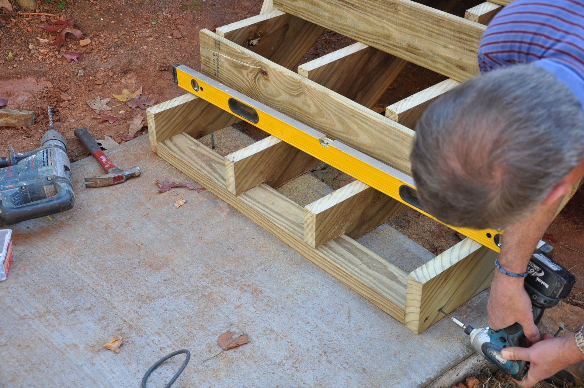 A floor buffer sits on a partially stained hardwood floor with three containers of stain nearby in a sunlit room.