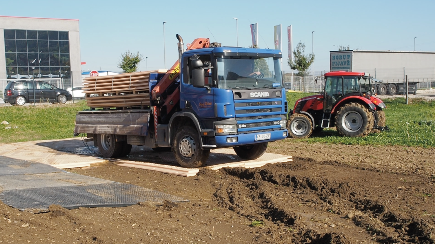 Un camión azul y un tractor rojo están estacionados en un campo de tierra.