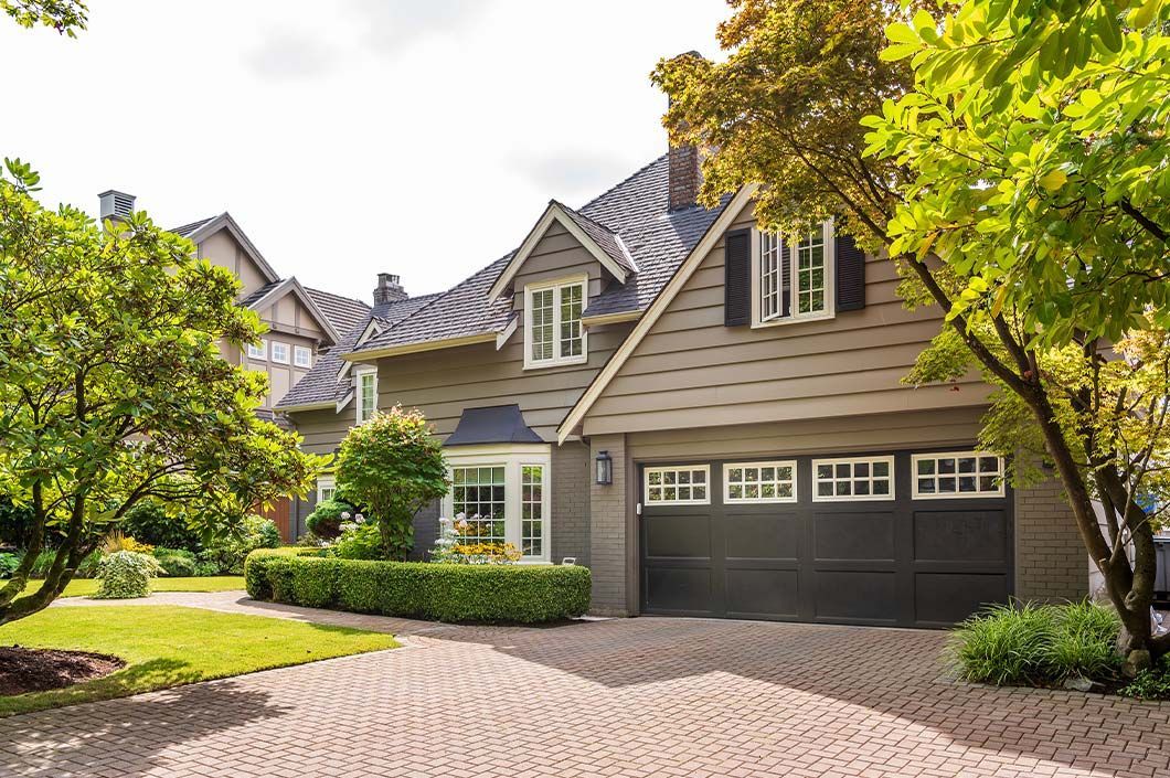 A large house with a black garage door and a brick driveway.