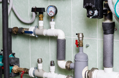 Plumbing pipes and valves on a tiled wall with a pressure gauge and insulated sections