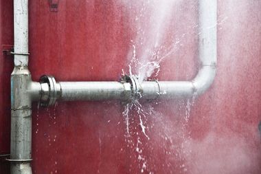 Leaking metal pipe spraying water against a red wall