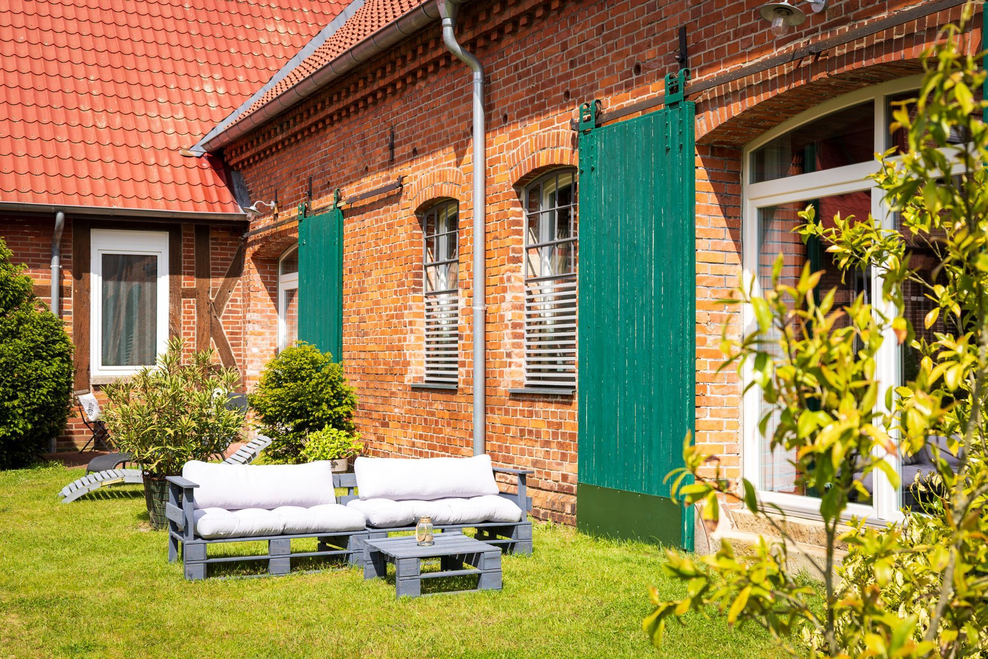 Backsteinhaus mit rotem Dach, grünen Fensterläden und einer weißen Bank auf einem sonnigen Rasen