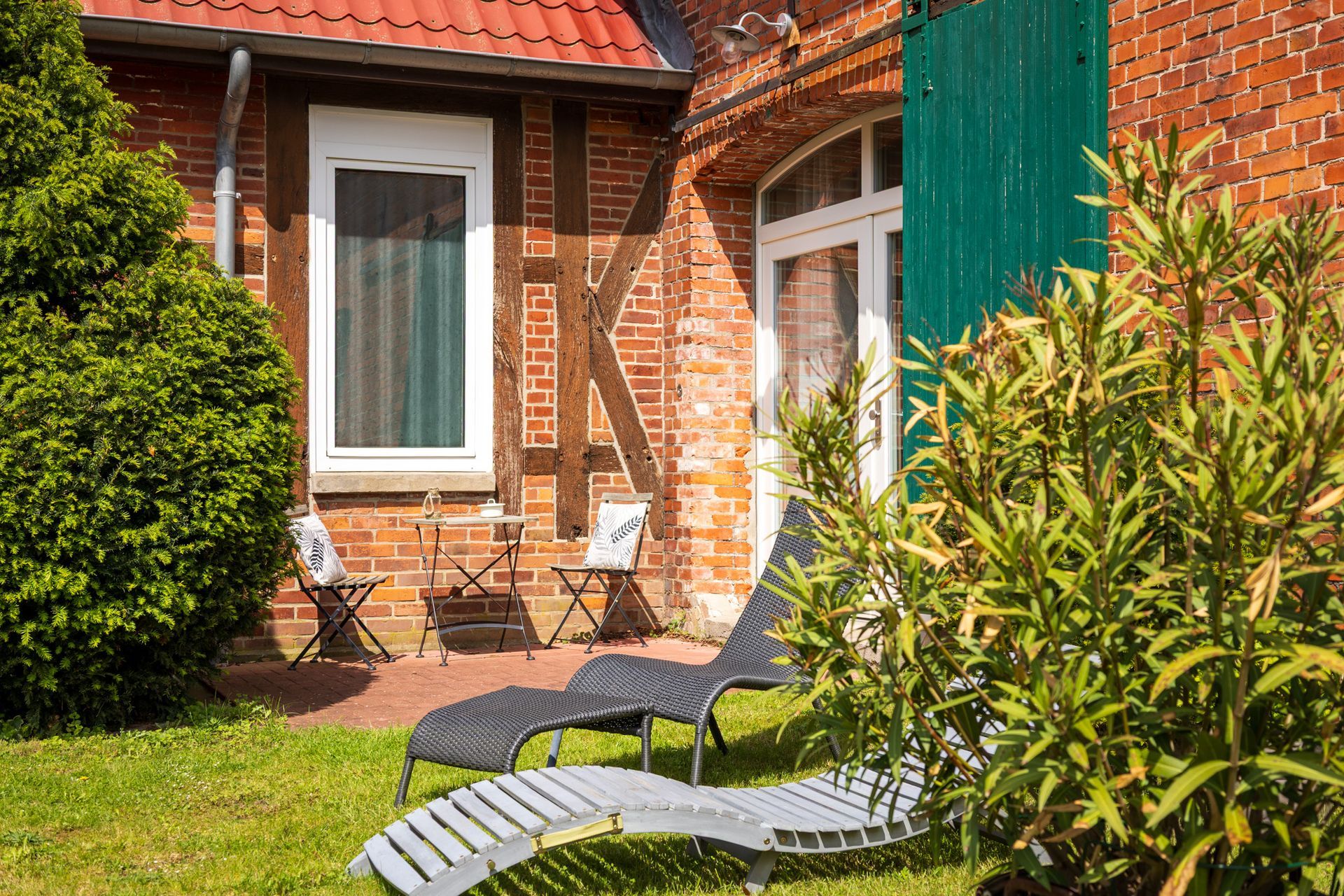 Terrasse am Backsteinhaus mit Liegestühlen und üppigen grünen Sträuchern in einem sonnigen Garten